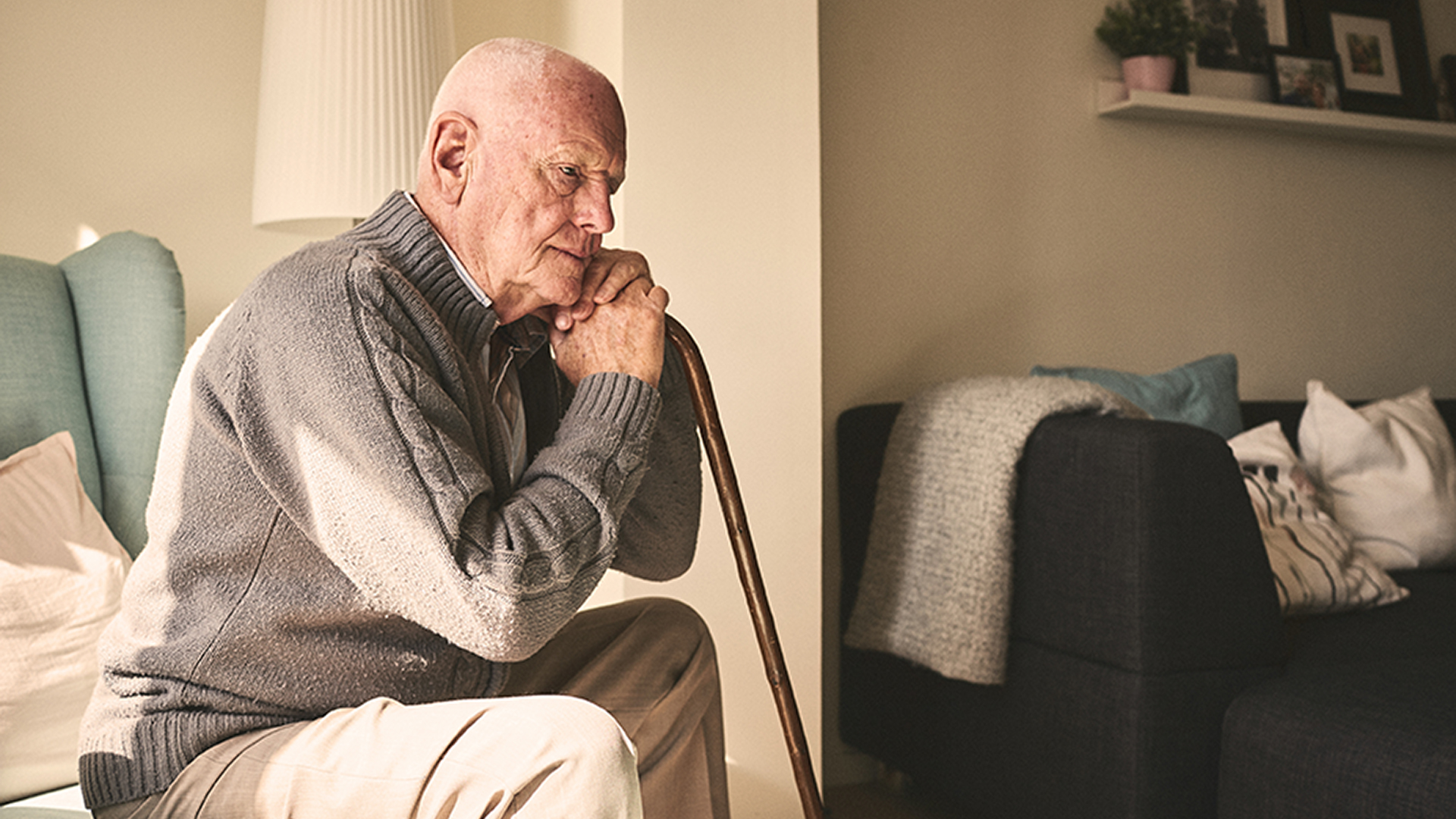 Thoughtful elderly man sitting alone at home with his walking cane