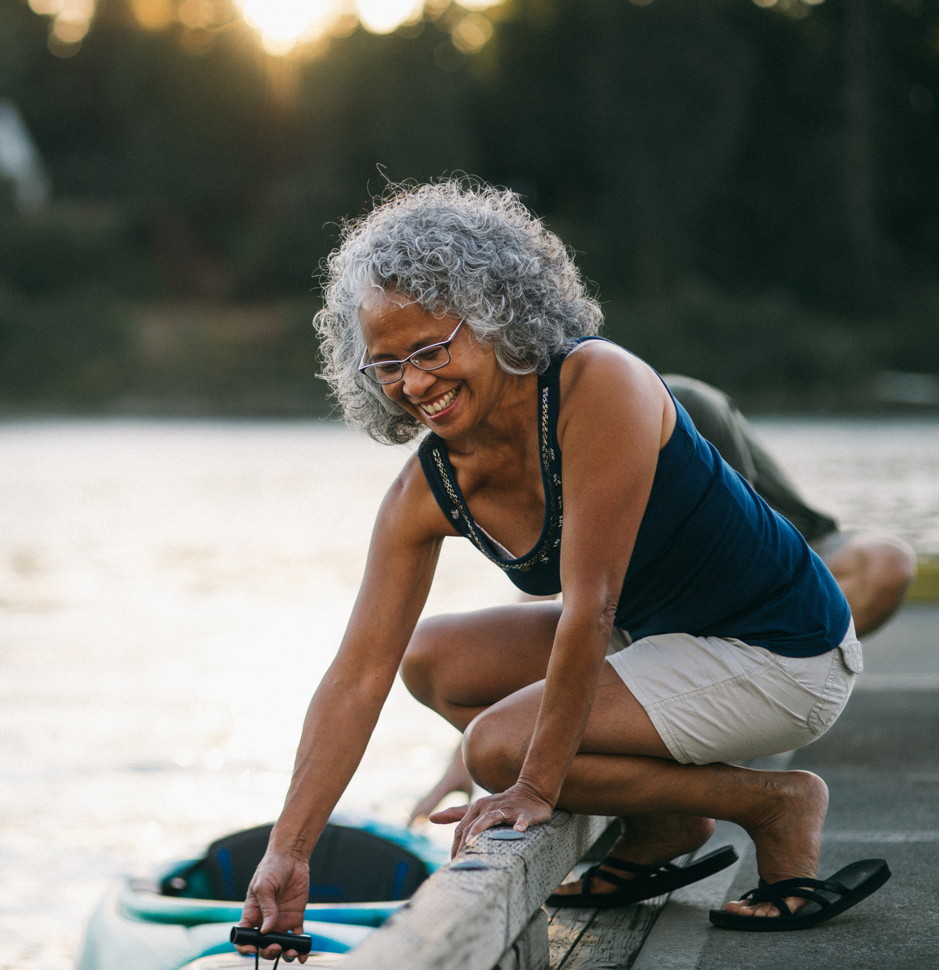 Cheerful senior woman preparing to kayak on river at sunset Senior preparing paddle board by waters edge.