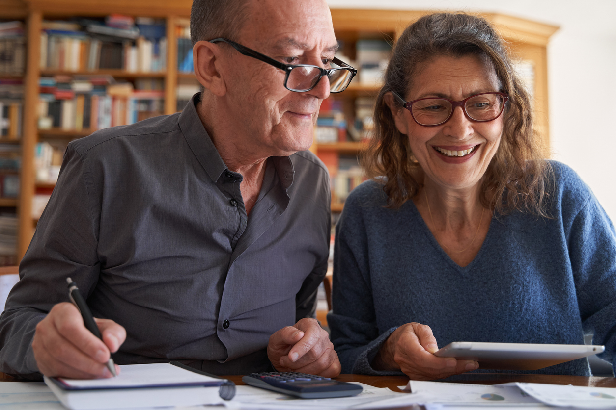 Annapolis senior couple with tablet and calculator smile while managing bills and paperwork. 