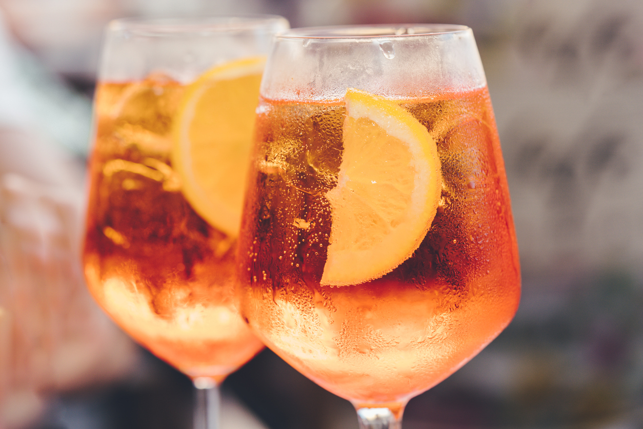 Glass of ice cold Spritz cocktail served in a wine glass, decorated with slices of orange.