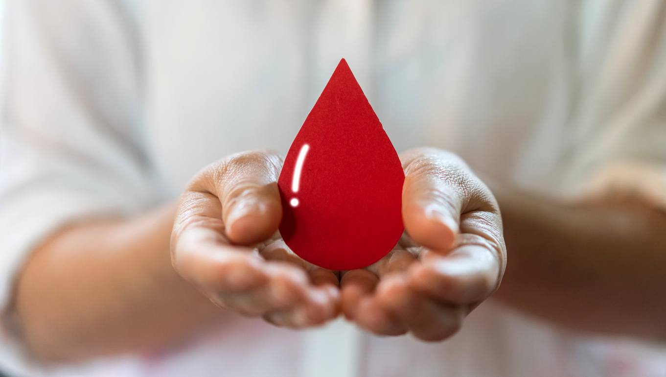 Hand holding red heart and blood drop.